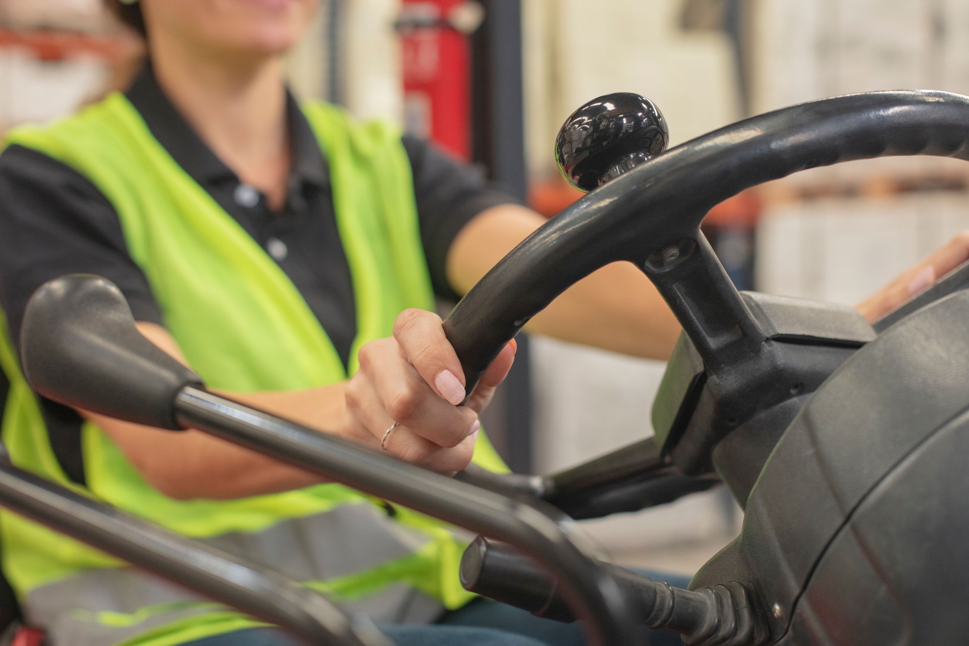 Detail of female employee wearing protective workwear and driving forklift at distribution warehouse